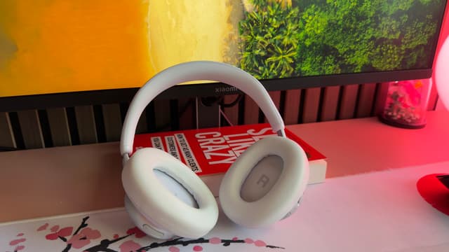 JBL Live 780NC i vitt stående på ett skrivbord framför en datorskärm